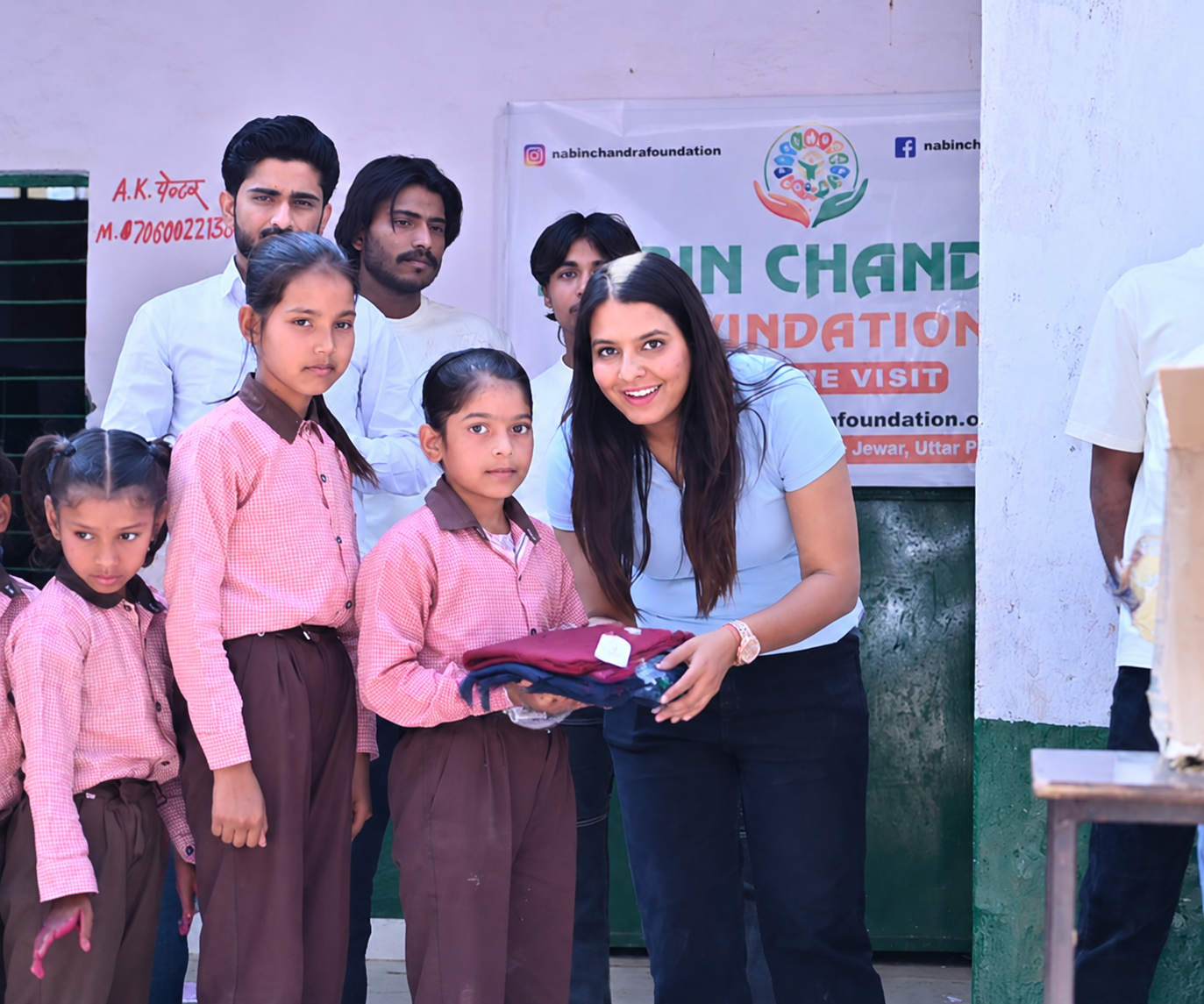 NCF volunteer handing folded clothing to a girl student outside a school as part of the clothing donation drive